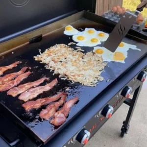 Breakfast cooking on a Blackstone griddle with bacon, hash browns, and sunny-side-up eggs.