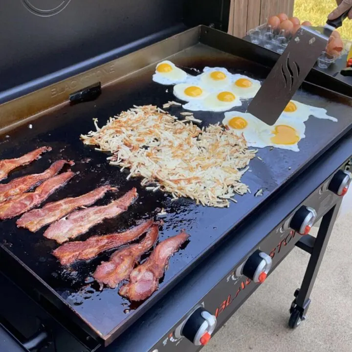 Breakfast cooking on a Blackstone griddle with bacon, hash browns, and sunny-side-up eggs.